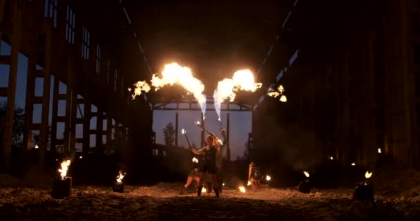Группа людей с огнем и факелами танцует на закате в ангаре в замедленной съемке. Огненное шоу — стоковое видео