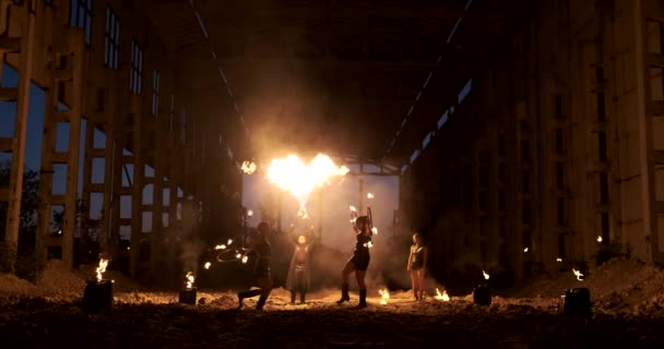 Quatro mulheres em roupas de couro com dança de fogo e show fire mostram um homem com um lança-chamas nas costas joga com a chama em câmera lenta . — Vídeo de Stock