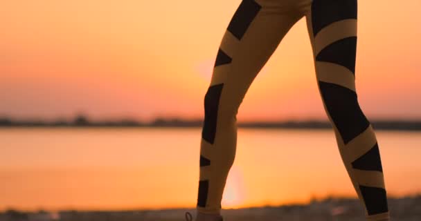 Una mujer realiza sentadas al atardecer en la playa en cámara lenta. Ejercitar los músculos de las caderas . — Vídeos de Stock