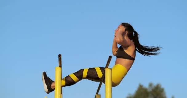 Fitte Mädchen trainieren Bauchmuskeln, indem sie die Beine auf einer Horisontalstange anheben. Fitnesstrainerin macht Übungen am See. — Stockvideo