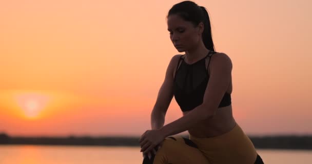 A woman performs sit-UPS at sunset on the beach in slow motion. Exercise the muscles of the hips. — Stock Video