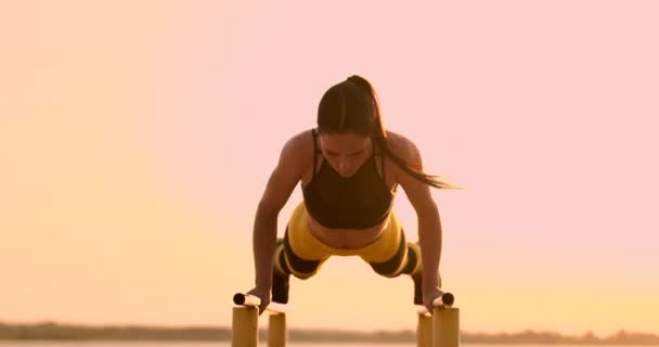 Красивая спортсменка на закате выполняет отжимания на параллельной горизонтальной полосе — стоковое видео