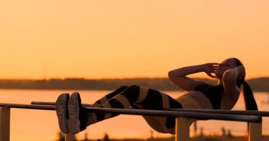 Çok sağlıklı ve formda kadının asılı bacak gerçekleştirme samimi atış sunset beach promenade, açık alan fitness istasyonda yükseltir. Gösteren güçlü karın altı kutu