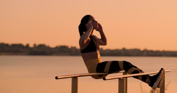 Porträtt av stark ung kvinna som hänger på väggen barer med benen. Fitness kvinna utför hängande benet höjer på utomhus. — Stockvideo