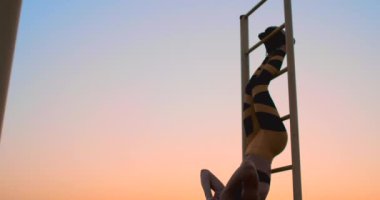 Bacaklarını çubuklarıyla duvara asılı güçlü genç kadın portresi. Fitness kadın asılı bacak performans üzerinde açık yükseltir.