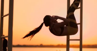 Çok sağlıklı ve formda kadının asılı bacak gerçekleştirme samimi atış sunset beach promenade, açık alan fitness istasyonda yükseltir. Gösteren güçlü karın altı kutu