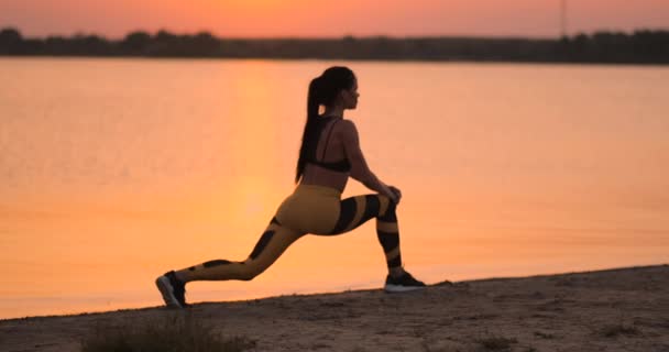 La donna sta facendo affondi e accovacciandosi all'aperto, addestrando il suo corpo. Giovane donna magra sta lavorando muscoli delle gambe, fianchi e glutei — Video Stock