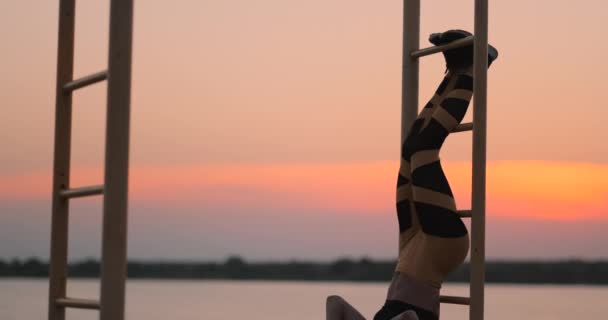 Upřímný záběr opravdu zdravé a fit ženy provádějící visící nohy zvýší na venkovní fitness stanice v západu slunce na plážovou promenádu. Zobrazeno silné břišní six-pack — Stock video