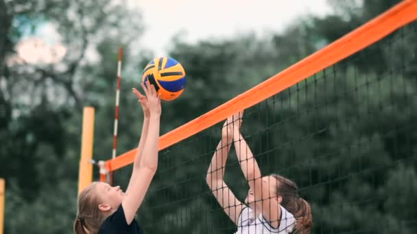 Junge Frau, die am Strand Volleyball spielt, in einem Team, das einen Angriff auf den Ball durchführt. Mädchen in Zeitlupe trifft den Ball und führt einen Angriff durch das Netz aus — Stockvideo