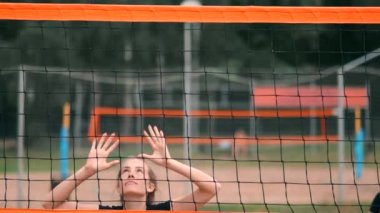 Yavaş Hareket, Yakın Çekim, Düşük Açı: Ağda voleybol oynayan tanınmayan genç kadın elleri. Hücum oyuncusu topu çiviler ve rakip bir turnuva sırasında topu sağ üstten engeller.