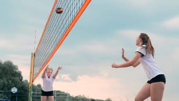 Молодая женщина играет в волейбол на пляже в команде, осуществляющей атаку удара по мячу. Девушка в замедленной съемке бьет по мячу и проводит атаку через сетку — стоковое видео