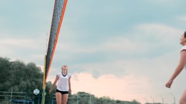 Plajda voleybol oynayan genç kadın atak gerçekleştiren bir takım topa vurdu. Yavaş çekimde kız topa vurur ve net üzerinden bir saldırı yürütmek