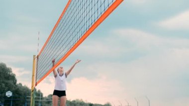 Plajda voleybol oynayan genç kadın atak gerçekleştiren bir takım topa vurdu. Yavaş çekimde kız topa vurur ve net üzerinden bir saldırı yürütmek