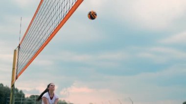 Plajda voleybol oynayan genç kadın atak gerçekleştiren bir takım topa vurdu. Yavaş çekimde kız topa vurur ve net üzerinden bir saldırı yürütmek