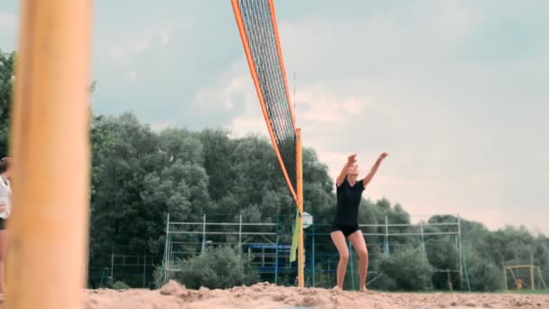 Mladá žena hrající volejbal na pláži v týmu, který provádí útok na míč. Dívka v pomalém pohybu zasáhne míč a provede útok sítí — Stock video