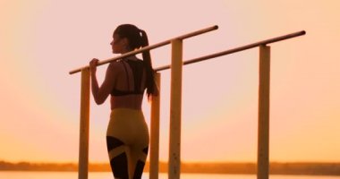 Gün batımı barında arka görüşe yakın bir yerde dinlenirken dinlenen kadın. Uzun saçlı güzel esmer bir kadın güneşte dinlenen yatay yatay çubuklar yakınında duruyor.