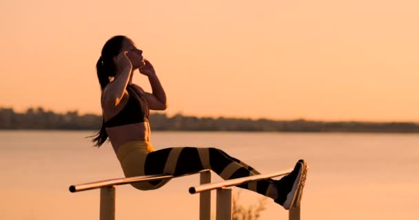 Portret van sterke jonge vrouw ophangen op muur balken met haar benen. Fitness vrouw uitvoeren van opknoping been werpt op buiten. — Stockvideo