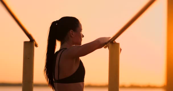 Mujer descansando mientras está de pie en la barra del atardecer cerca de la vista trasera. Una hermosa morena con el pelo largo se para cerca de las barras horizontales horizontales descansando al sol . — Vídeo de stock