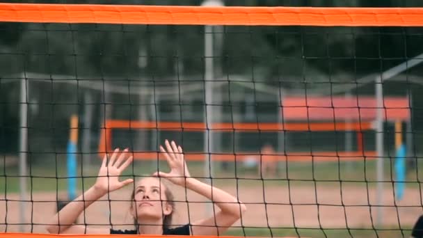 Pomalý pohyb, zavřít, nízký úhel: neidentifikovatelný mladý ženský ruce hrající volejbal na netu. Útočný hráč hřeje míč a protivník ho blokuje přímo nad sítí během turnaje.