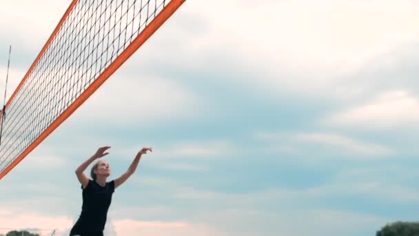 Mujer joven jugando voleibol en la playa en un equipo llevando a cabo un ataque golpeando la pelota. Chica en cámara lenta golpea la pelota y llevar a cabo un ataque a través de la red — Vídeo de stock
