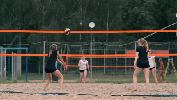 Молода жінка грає у волейбол на пляжі в команді, яка здійснює напад на м'яч. Дівчина в повільному русі потрапляє в м'яч і здійснює атаку через мережу — стокове відео