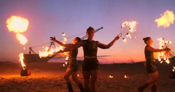 Fire show three women in their hands twist burning spears and fans in the sand with a man with two flamethrowers in slow motion. — Stock Video