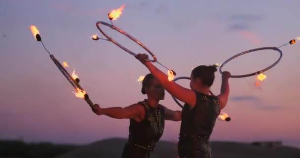 Frauen mit Feuer bei Sonnenuntergang auf dem Sand tanzen und zeigen Tricks gegen den schönen Himmel in Zeitlupe. — Stockvideo