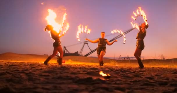 Artistas profissionais mostram um show de fogo em um festival de verão na areia em câmera lenta. acrobatas quarta pessoa de trabalho de circo com fogo à noite na praia . — Vídeo de Stock