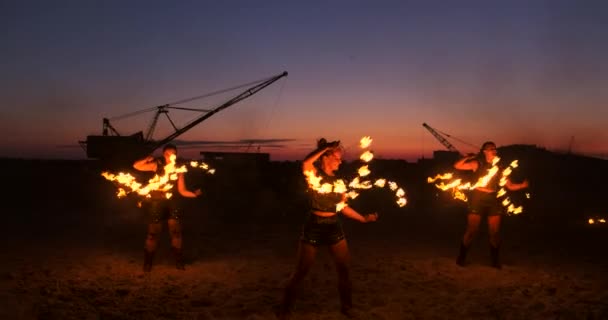Een groep mannen en vrouwen vuurshow 's nachts op het zand tegen de achtergrond van vuur en torenkranen — Stockvideo