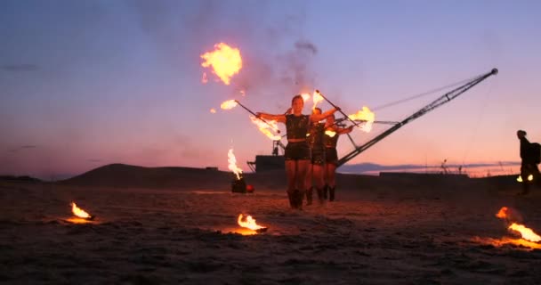 Група чоловіків і жінок пожежного шоу вночі на піску на тлі вогню і баштових кранів — стокове відео