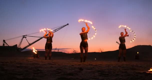Fire show tre kvinnor i sina händer twist brinnande spjut och fläktar i sanden med en man med två eldkastare i slow motion. — Stockvideo