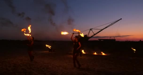 Un grupo de hombres y mujeres espectáculo de fuego en la noche en la arena sobre el fondo de fuego y grúas torre — Vídeo de stock