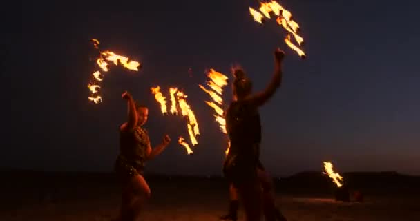 プロのアーティストは、スローモーションで砂の上の夏祭りで火のショーを示しています。ビーチで夜に火でサーカスの仕事から4人目のアクロバット. — ストック動画