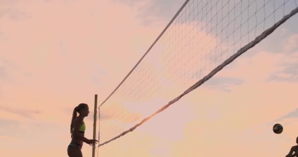 Jovens jogadoras de voleibol do sexo feminino passam e espetam a bola sobre a rede em uma noite de verão ensolarada. Ajuste meninas caucasianas jogando vôlei de praia ao pôr do sol — Vídeo de Stock