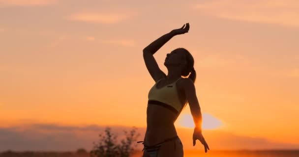 スローモーションでボールに背中を置く日没時のミドルプランの女性バレーボール選手 — ストック動画