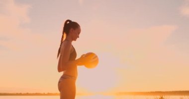 Plaj voleybolu oynayan atletik kız havada atlar ve güzel bir yaz akşamı net üzerinden topa vurur. Beyaz kadın bir puan