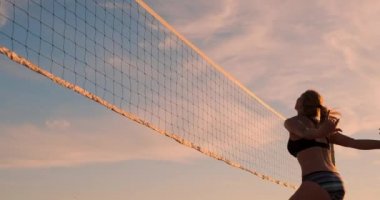 Plaj voleybolu oynayan atletik kız havada atlar ve güzel bir yaz akşamı net üzerinden topa vurur. Beyaz kadın bir puan