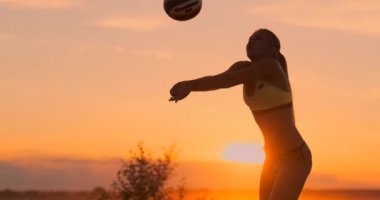 Yavaş Hareket, Düşük Açı, Close Up, Sun Flare: Plaj voleybolu oynayan atletik kız havada atlar ve güzel bir yaz akşamı net üzerinden topa vurur. Beyaz kadın bir puan