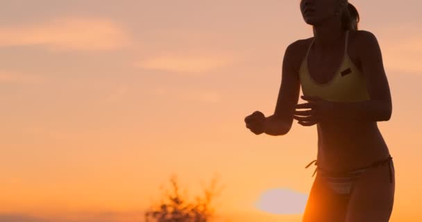 Medeldistans volleyboll flicka i bikini väntar på bollen på banan vid solnedgången ger underarm passera under en match på stranden i slow motion — Stockvideo