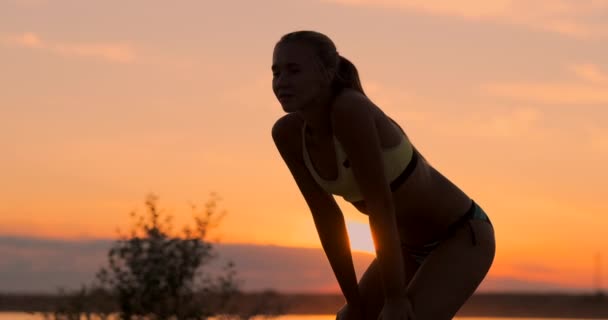 Athletic girl playing beach volleyball jumps in the air and strikes the ball over the net on a beautiful summer evening. Caucasian woman score a point — Stock Video