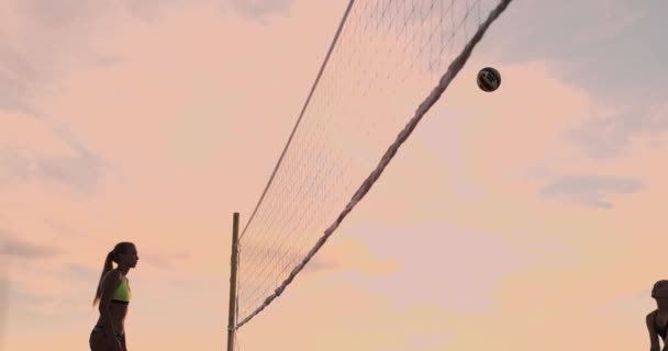 Beachvolleybal wedstrijd meisjes raken de bal in slow motion bij zonsondergang op het zand. — Stockvideo