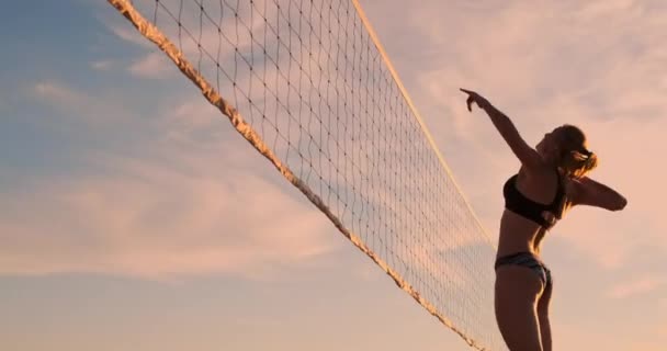 スローモーションで日没時に砂の上で夏のバレーボールでビーチで遊ぶビキニのセクシーなバレーボールの女の子. — ストック動画