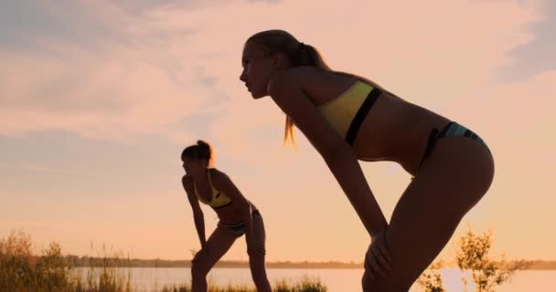 Jóvenes jugadoras de voleibol pasan y clavan la pelota sobre la red en una soleada noche de verano. Ajuste chicas caucásicas jugando voleibol de playa al atardecer — Vídeos de Stock