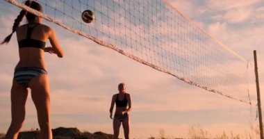 Genç kadın voleybolcular güneşli bir yaz akşamı pas ve net üzerinden topu başak. Fit Kafkas kızlar gün batımında plaj voleybolu oynuyor