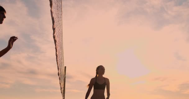 LOW MOTION, LOW ANGLE, CLOSE UP, SUN FLARE: Menina atlética jogando vôlei de praia salta no ar e bate a bola sobre a rede em uma bela noite de verão. Mulher branca marcar um ponto — Vídeo de Stock