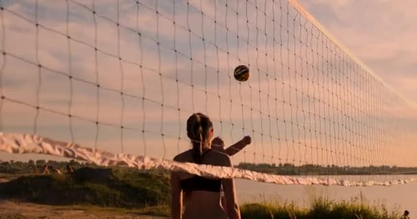 Slow motion, låg vinkel, närbild, sol flare: atletisk flicka som spelar beachvolleyboll hoppar i luften och slår bollen över nätet på en vacker sommarkväll. Kaukasiska kvinna poäng en punkt — Stockvideo