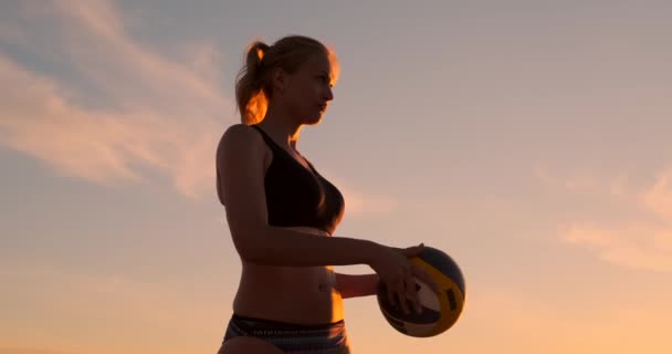 Krásná žena v bikinách s míčem při západu slunce se připraví na skok na pláži ve volejbalové sirtě na písku. — Stock video