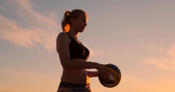 Une belle femme en bikini avec une balle au coucher du soleil se prépare à servir saut sur la plage dans un match de volley-ball sur le sable . — Video