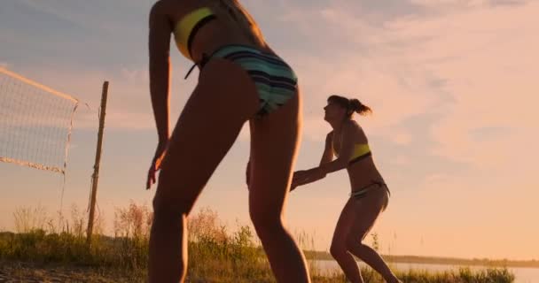 LOW MOTION, LOW ANGLE, CLOSE UP, SUN FLARE: Menina atlética jogando vôlei de praia salta no ar e bate a bola sobre a rede em uma bela noite de verão. Mulher branca marcar um ponto — Vídeo de Stock