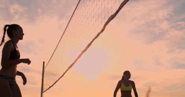 LOW MOTION, LOW ANGLE, CLOSE UP, SUN FLARE: Menina atlética jogando vôlei de praia salta no ar e bate a bola sobre a rede em uma bela noite de verão. Mulher branca marcar um ponto — Vídeo de Stock